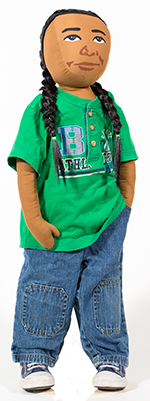 AmazeWorks Persona Doll, Simon, wearing his hair in two long black braids, a green graphic t-shirt, blue jeans, and blue and white sneakers. 