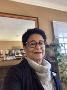 Candace Whittaker smiling wearing glasses, a gray turtleneck, and a black jacket.