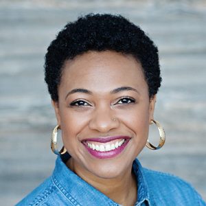 a headshot of Marcee Harris smiling, wearing gold hoop earrings, a chambray shirt, and pink lipstick.