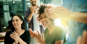 Four coworkers enthusiastically laugh, smile, and applaud in a sun-drenched conference room