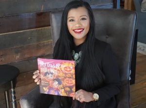 Thuba Nguyen wearing black and smiling, holding the children's book she wrote entitled, "My Daddy Tells Me"