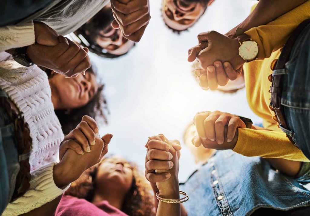 A group of 6 people standing in a circle, holding hands, shot from below.