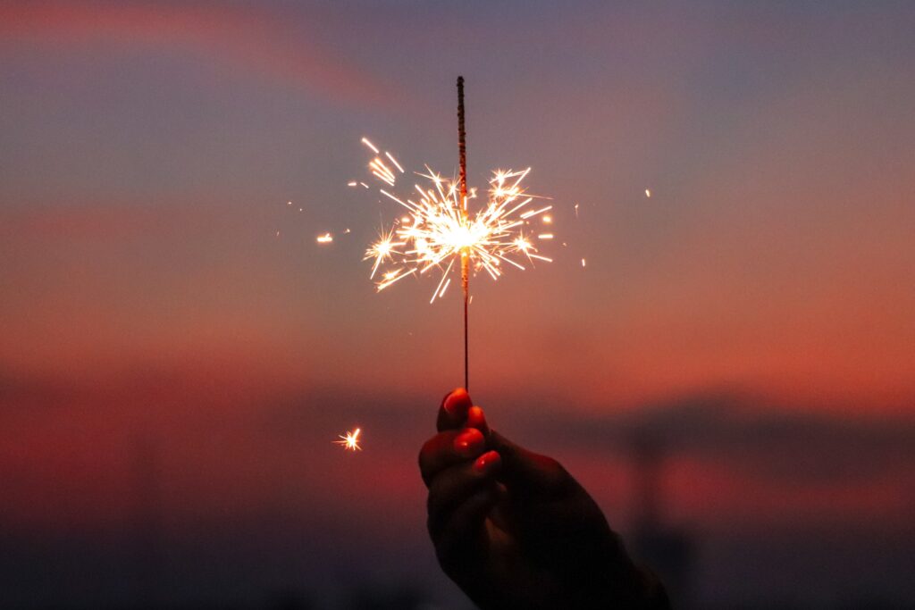 a hand holding up a sparkler with a sunset in the background