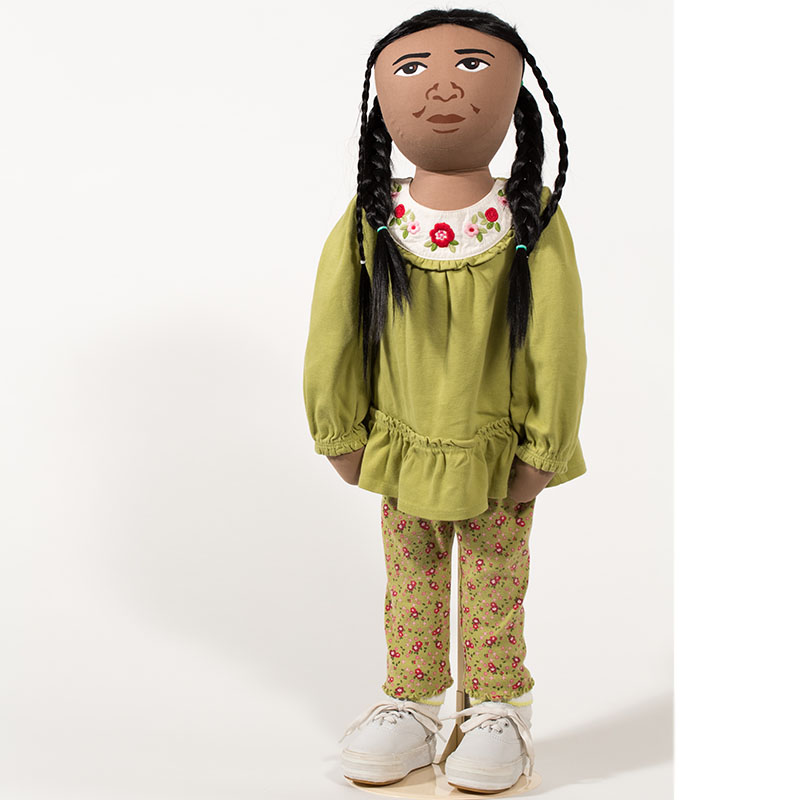 AmazeWorks Persona Doll, Leela, wearing a green shirt and pants with red flowers on them, white tennis shoes, and four braids in her hair - two thin face-framing braids, and two thick braids.