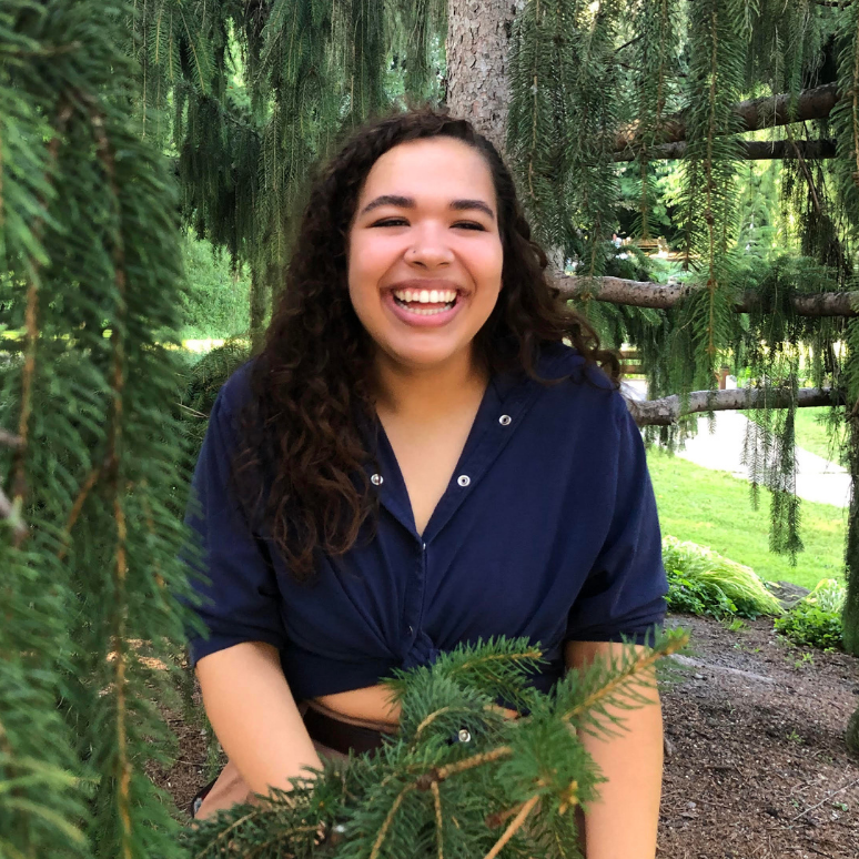Sidra Michael smiling while surrounded by pine leaves
