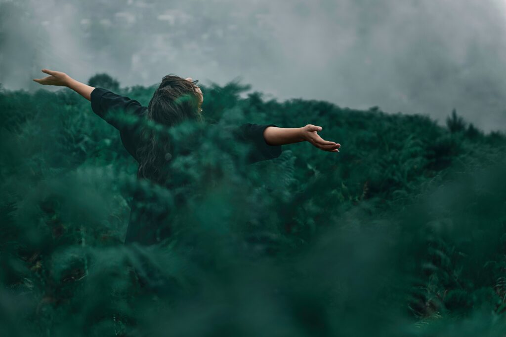 A person in the woods facing away from the camera and reaching their arms out