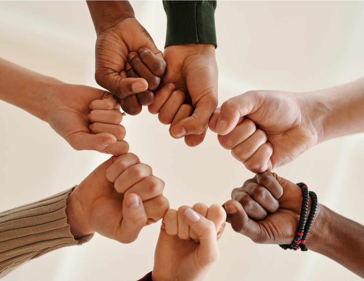 7 people of different skin colors holding closed fists together in a circle
