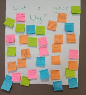 A white poster titled, "What is your Why?" covered in multi-colored post-it notes with educators' reasons for joining the teaching profession