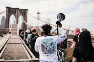 Many protesters walking the Brooklyn Bridge. One carries a megaphone.