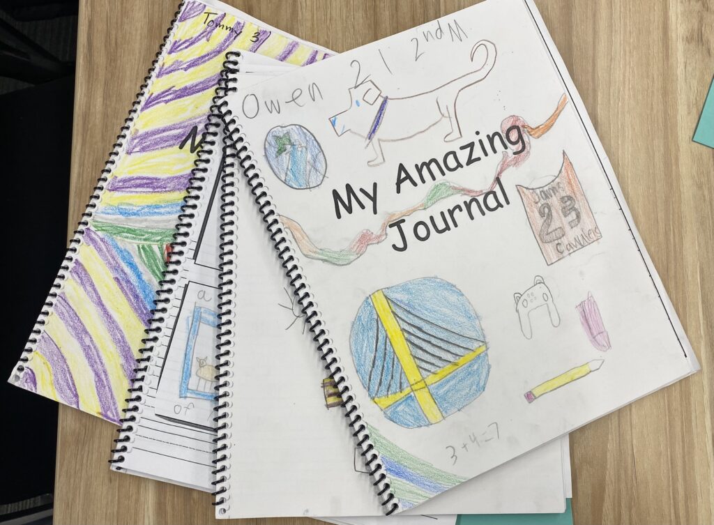 Four children's journals stacked in a spiral. The top reads, "My Amazing Journal" with a child's drawings of a dog, bridge, pencil, and other images. 