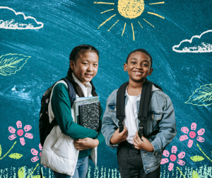 Two middle school students wearing backpacks and holding books in front of a chalk drawn background of a sky, sun, clouds, grass, and flowers