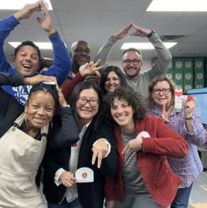 AmazeWorks board smiling and creating the letter "A" with their hands. They hold up AmazeWorks stickers and bookmarks.