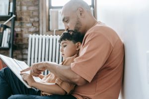 A father reads a book with his son, pointing to one of the pages