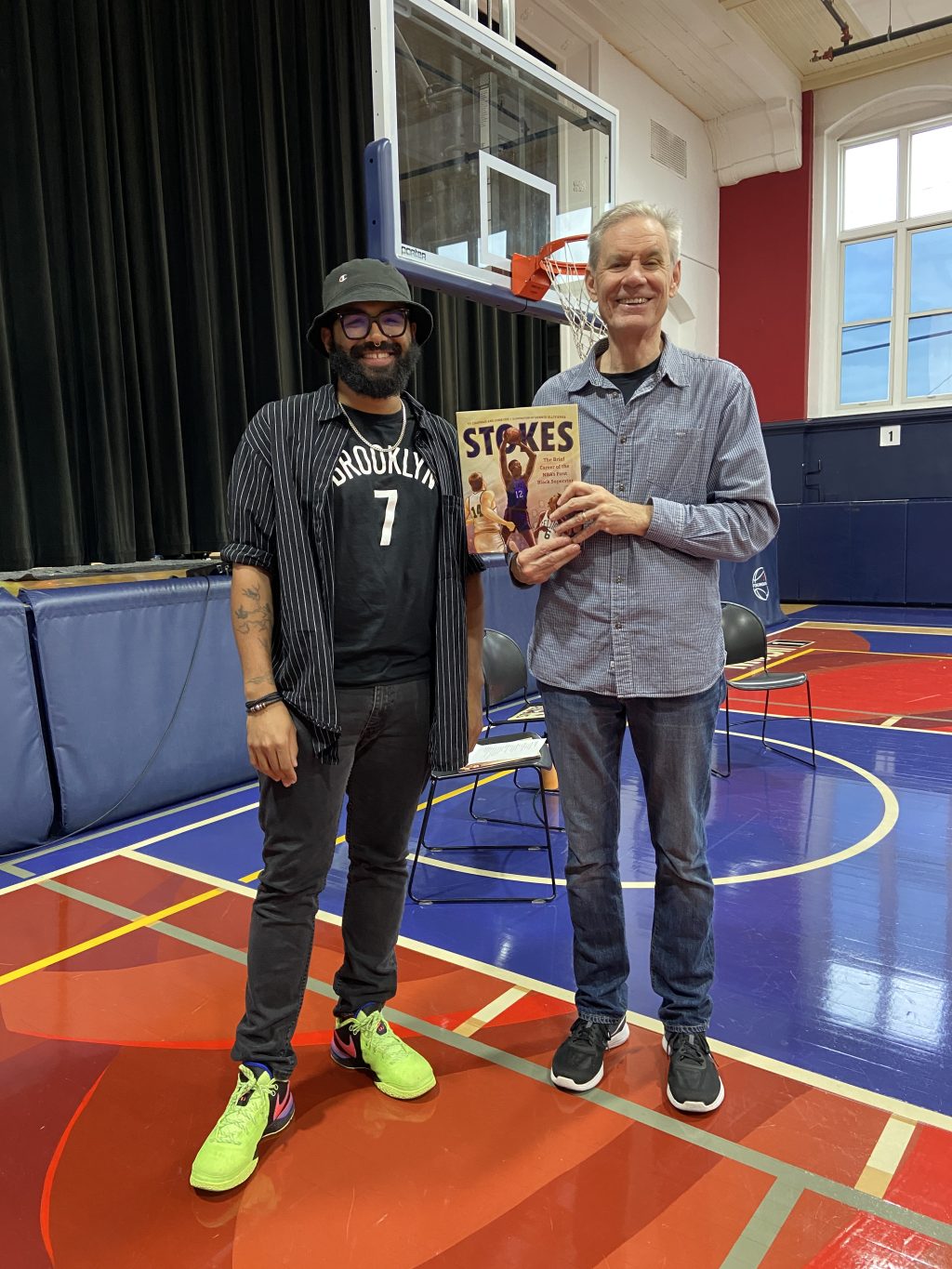 Ty Chapman and John Coy smiling and holding a copy of STOKES while standing on a basketball court