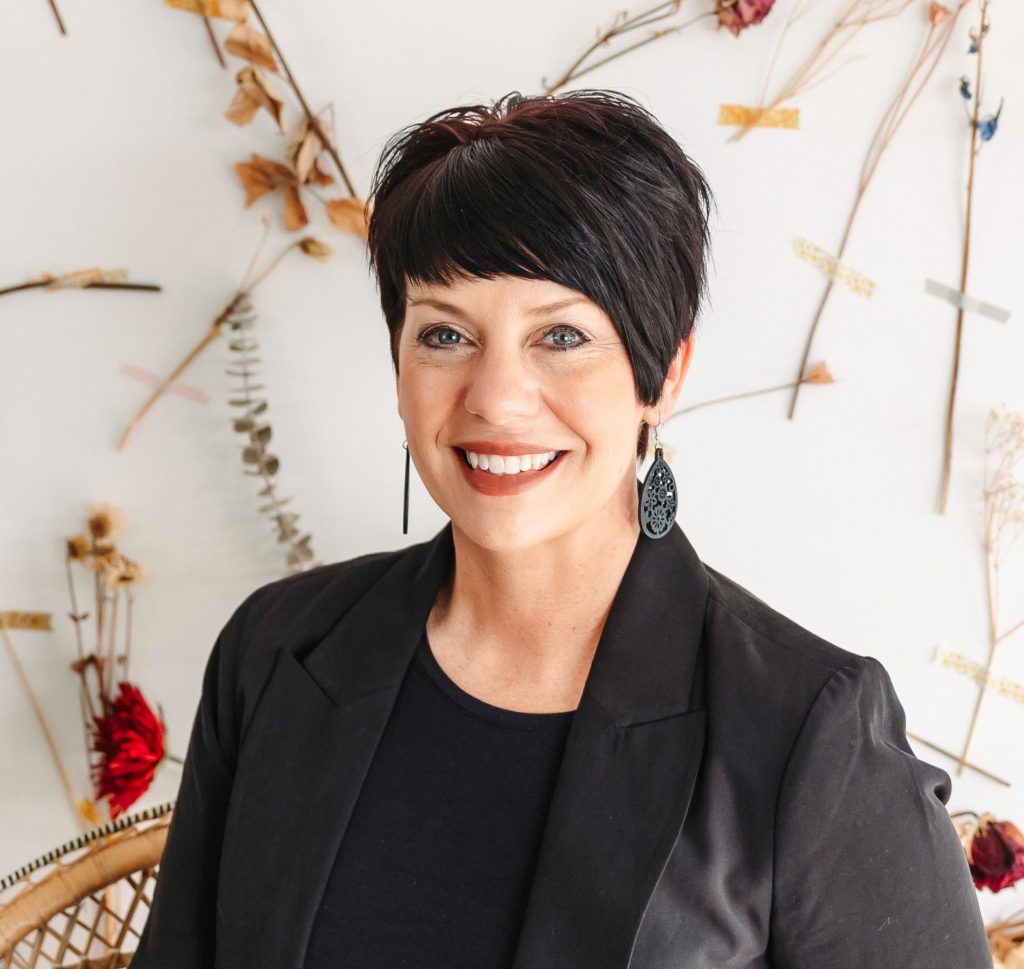 Headshot of Erin Rathke, a White woman with short black hair, smiling and wearing a black shirt and blazer.