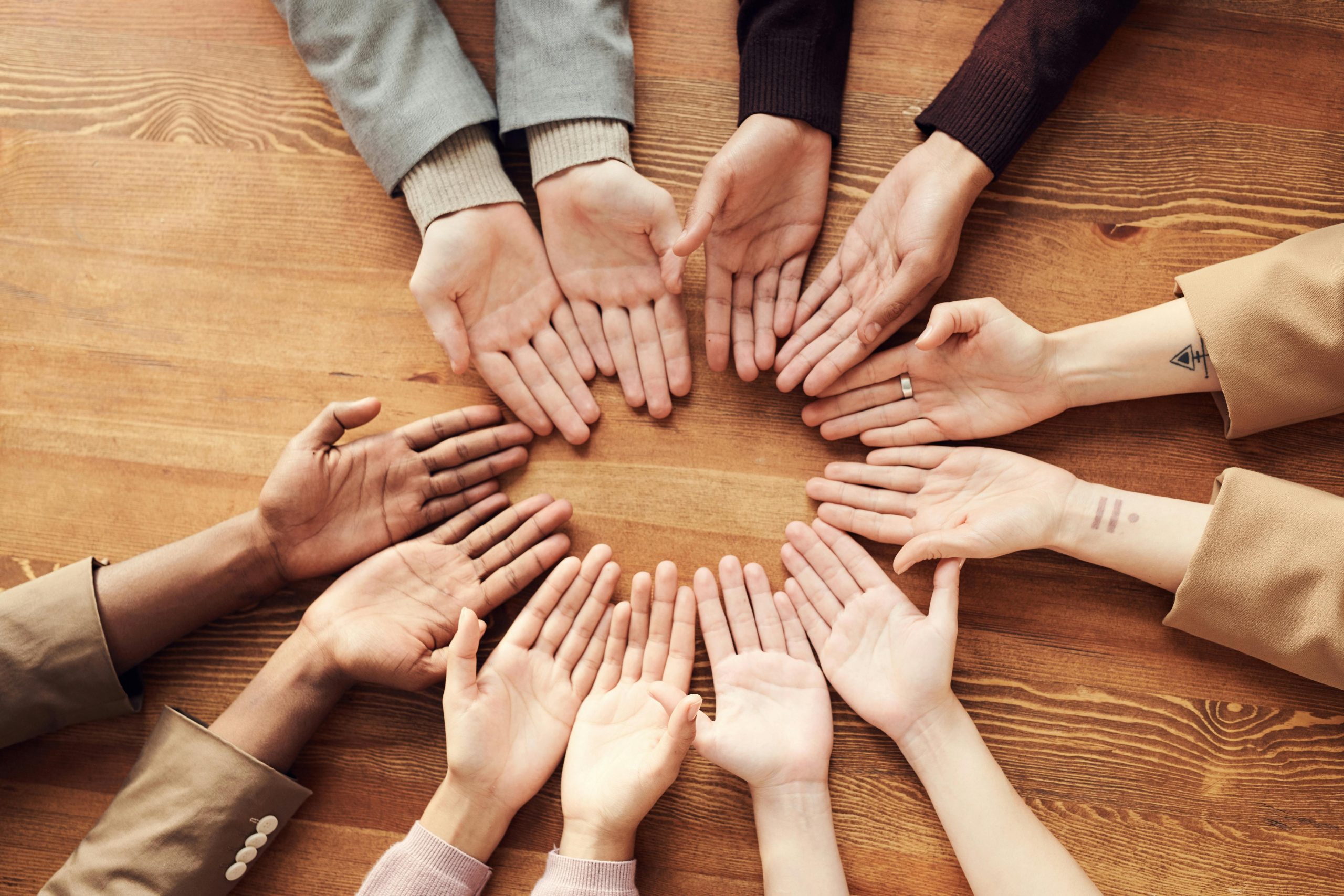 Six people's hands facing palm up, formed in a circle on a wooden table