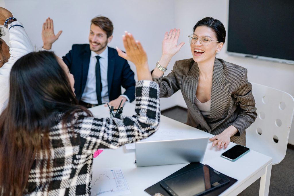 Four employees sitting at a work table smiling and high fiving