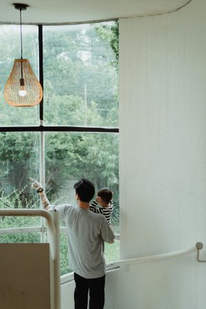 a father holds his child and points outside, looking out a large window