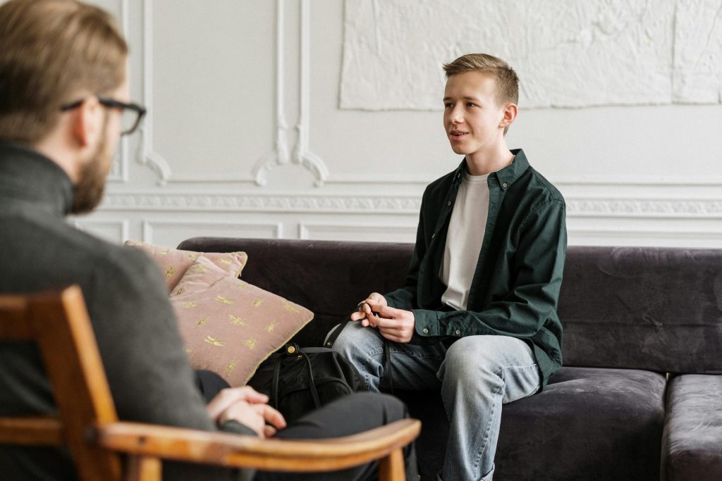 A white boy sits on a couch talking to a therapist