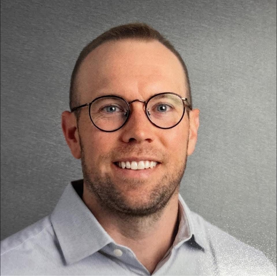 Scott Sundstrom is smiling. He is a white man wearing a button-down shirt and black glasses.