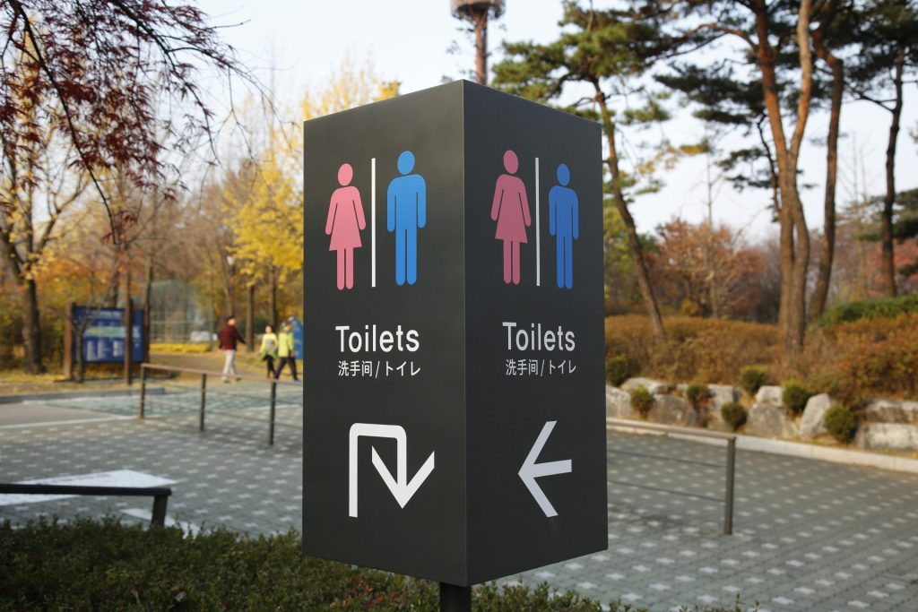 A bathroom sign in a park pictures a pink figure in a dress and a blue figure in pants