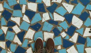 A pair of brown shoes standing on a floor that is a mosaic of dark blue, light blue, and white tiles.