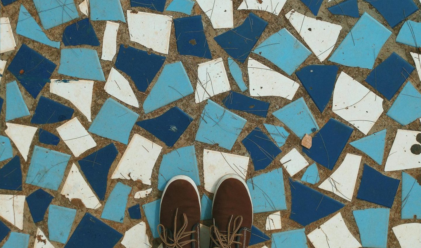 A pair of brown shoes standing on a floor that is a mosaic of dark blue, light blue, and white tiles.