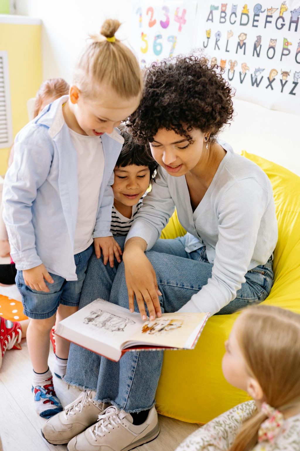 A teacher reads a book to two children in her classroom