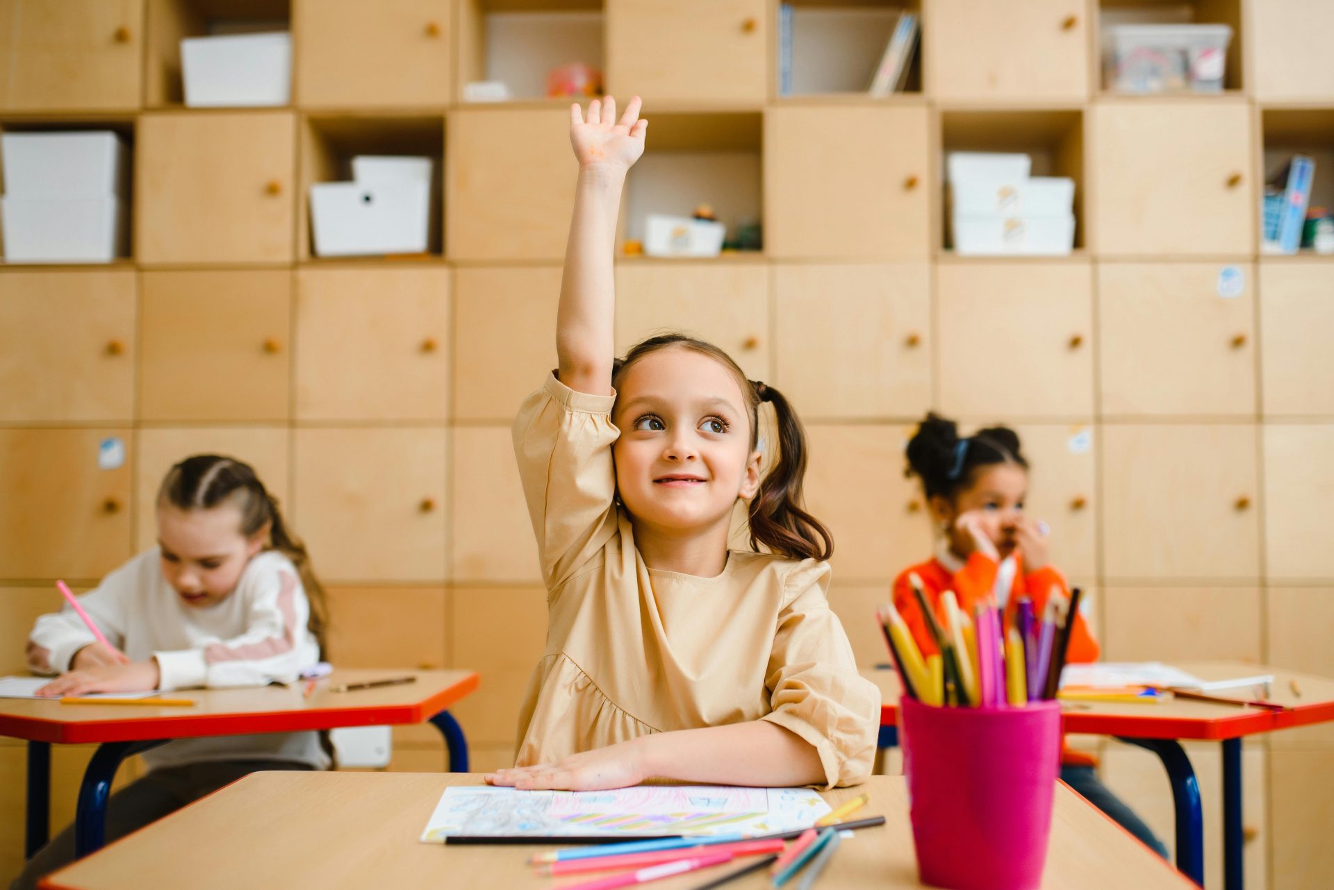 A child raises her hand in a classroom