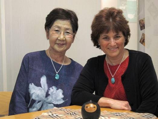 Sachiko Yasui and Caren Stelson smiling together. They wear matching necklaces with a blue stone.