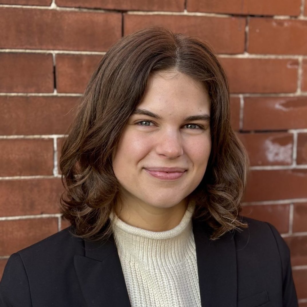 Sophie Herrington headshot - a White wmoan with brown hair, wearing a black blazer with a white sweater
