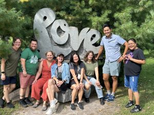 AmazeWorks staff smiling next to a "Love" sculpture