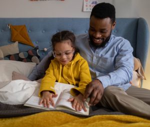 A father reads a book with his daughter in bed